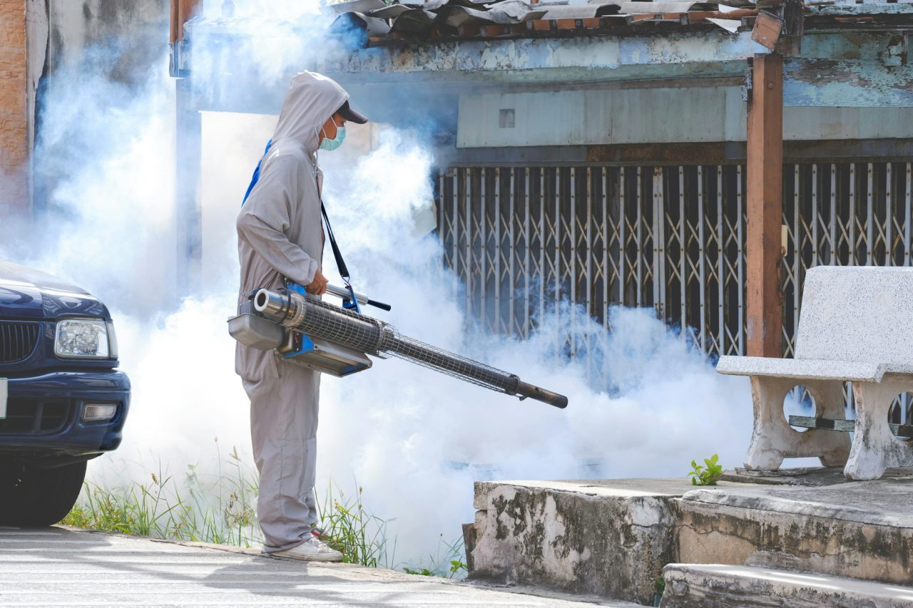 Healthcare worker spraying chemical to eliminate mosquitoes in overgrown area at abandoned house